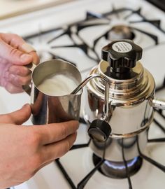 a person is pouring milk into a coffee pot on the stove top, while another hand reaches for something