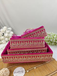 three pink and gold boxes sitting on top of a bamboo mat next to white flowers