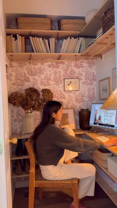 a woman sitting at a desk in front of a computer monitor and keyboard, with books on the shelves behind her