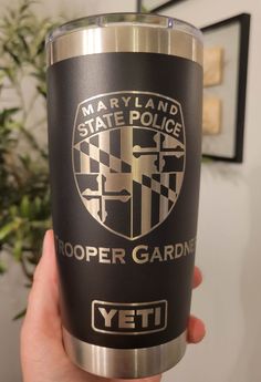 a person holding up a black and silver yeti tumbler that says, maryland state police trooper garden