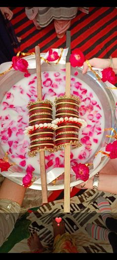 two people holding plates with flowers on them and wooden skewers in the middle