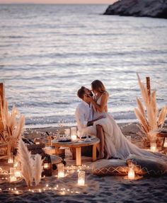 two people sitting on a table with candles in front of them and the water behind them