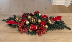 a christmas arrangement with poinsettis, bells and bows on a wooden table