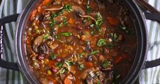 a pot filled with stew and vegetables on top of a striped cloth next to spoons