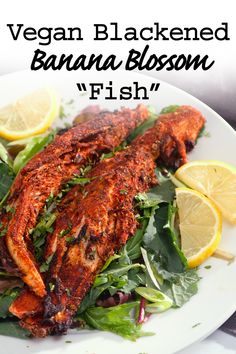 a white plate topped with fish next to lemon wedges and spinach leafy greens