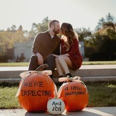 an engaged couple kissing in front of pumpkins that say we're expecting on them