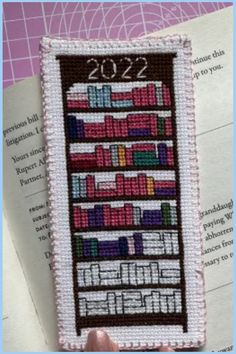 someone is holding up a cross stitch bookmark with books on the front and back