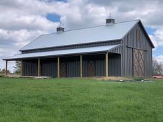 a large black barn sitting on top of a lush green field