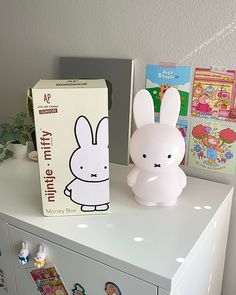 a white bunny sitting on top of a dresser next to a box and some children's books