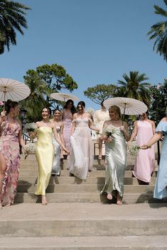 a group of women in dresses walking up some steps with umbrellas over their heads