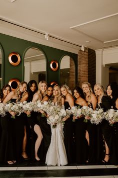 a group of women standing next to each other in front of a green wall holding bouquets