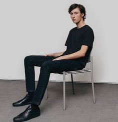 a man sitting in a chair with his legs crossed on the ground and wearing black shoes