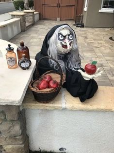 a creepy doll sitting on top of a stone wall next to an apple basket and bottles