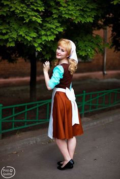 a woman dressed in a costume standing on the street with her hands up and smiling