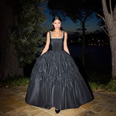 a woman in a long black dress standing on a stone walkway at night with trees and water in the background