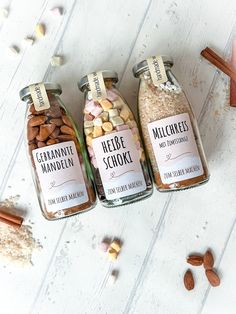 three jars filled with different types of nuts on top of a white table next to cinnamons