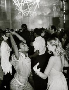 black and white photograph of people dancing at a party with lights in the ceiling behind them