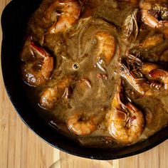 a skillet filled with shrimp and gravy on top of a wooden table