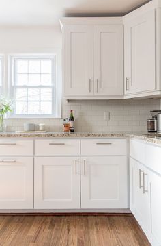 a kitchen with white cabinets and marble counter tops is pictured in this image, there are two vases on the window sill