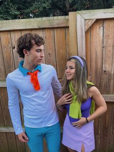 a man and woman dressed up in costume standing next to each other near a fence