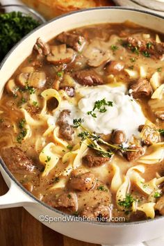 a large pot filled with pasta and meat soup on top of a wooden table next to bread