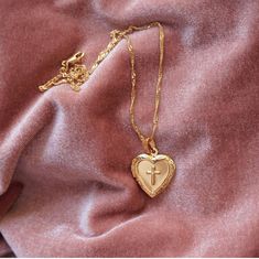 a gold necklace with a heart shaped pendant hanging from it's side on a pink cloth