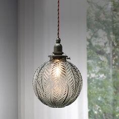 a glass light hanging from a ceiling in a room with white walls and trees behind it