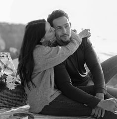 a man and woman sitting on the ground with their arms around each other while kissing