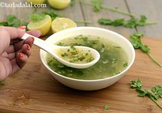 a person holding a spoon over a bowl filled with soup and garnished with cilantro