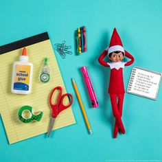 an elf doll sitting on top of a notepad next to scissors and other office supplies