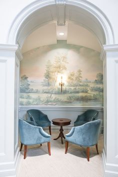 two blue chairs sitting in front of a wall with a painting on it's side