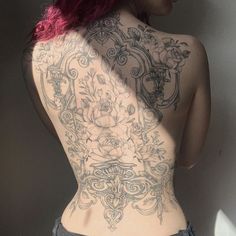 a woman with pink hair and tattoos on her back is standing in front of a wall