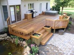 a wooden deck with steps leading to a hot tub and bbq grill in the back yard