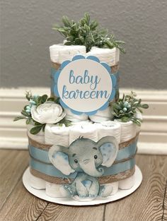 a baby shower cake with an elephant on top and greenery around the edges, sitting on a wooden table