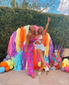 two women standing next to each other in front of a colorful backdrop with balloons and streamers