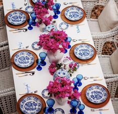 the table is set with blue and white plates, pink flowers, and silverware