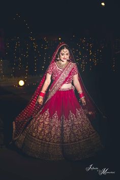 a woman in a red and gold lehenga is walking through the street at night