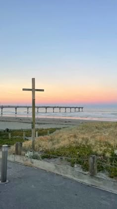 a wooden cross sitting on the side of a road next to the ocean at sunset