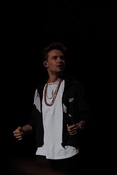 a man standing in front of a black background wearing a white t - shirt and necklace