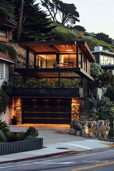 a large house with lots of windows and plants on the roof, next to a steep hill