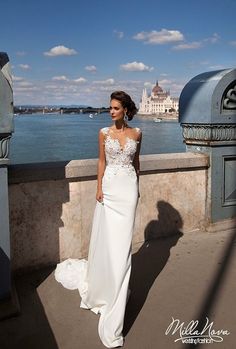 a woman in a white wedding dress standing on a bridge near the water and looking off into the distance