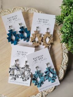 four earrings are sitting on a table next to some cards and a potted plant