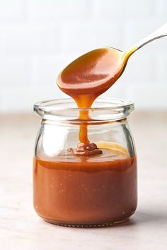 a spoon full of caramel sauce being poured into a jar