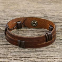 a close up of a leather bracelet on a wooden table with a metal button in the center