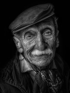 an old man with a hat and tie is looking at the camera in black and white