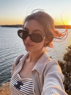 a woman taking a selfie with the sun setting in the background and water behind her