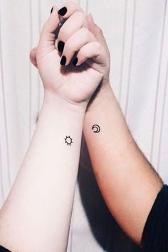 two people holding hands with tattoos on their arms and one has a sun and moon