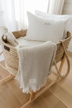 a baby's bed with a white blanket and teddy bear in the basket next to it