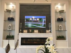 a television mounted on the wall above a fireplace in a living room with white flowers