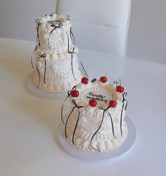 two cakes with white frosting and red cherries on them sitting on a table